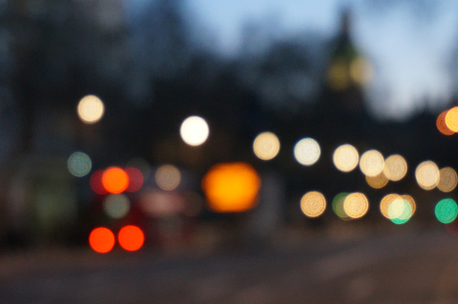 A blurred night cityscape with bokeh lights in warm and cool tones, including red, orange, and green circular light spots, evoking a quiet, reflective mood